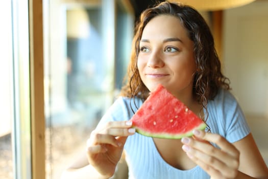 Happy woman eating watermelon sitting in a restaurant