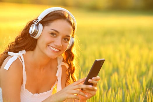 Happy woman wearing headphones listening music looks at you in a field