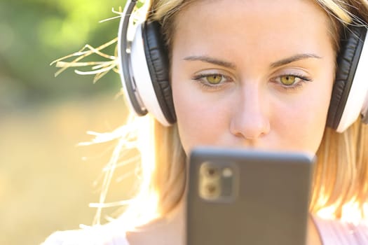 Front view portrait of a teen listening to music checking phone outside