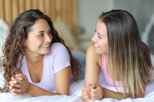 Two happy friends talking lying on the bed in a bedroom