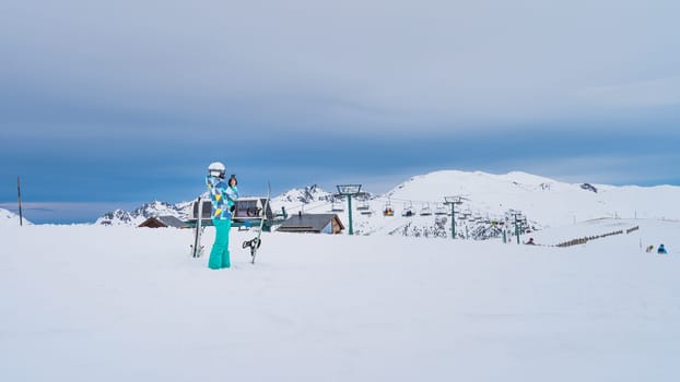 Woman skier taking a picture of a ski lift on the top of snowy Pyrenees Mountains. Skis planted in deep snow. El Tarter, Grandvalira, Andorra