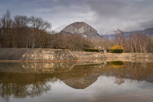 Panorama with mountain peak and trees reflecting in artificial pond, Pyrenees Mountains, Tarascon sur Ariege, France