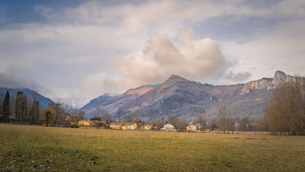 Surba town hiding behind trees at the foothill of Pyrenees Mountains with snowy peaks in background, Tarascon sur Ariege, France