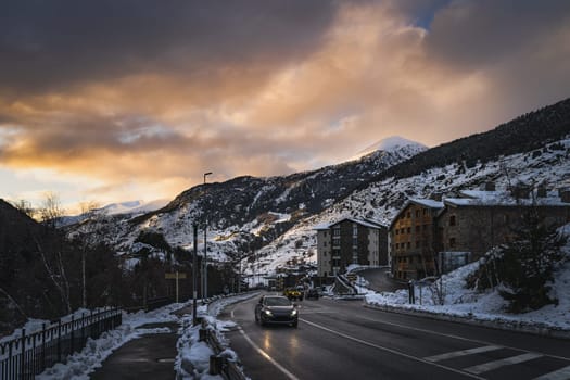 Cars on the road leading to El Tarter village after dusk. Sunset with sunlight illuminating mountain peaks in Pyrenees mountains, Grandvalira, Andorra