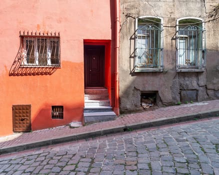 Exterior facade of old residential building with walls painted in orange, and wrought iron windows, at a narrow cobblestone street, Balat district, Istanbul, Turkey