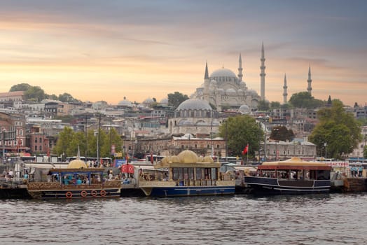 Istanbul, Turkey - August 25, 2022: Traditional fast food bobbing boats serving fish sandwiches at Eminonu square with Rustem Pasha Mosque and Suleymaniye Mosque in the background before sunset