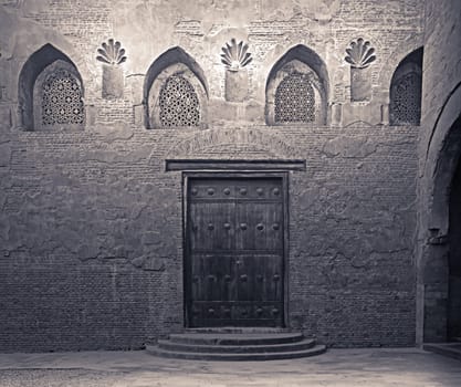 Aged wooden weathered door, perforated arched stucco window decorated with floral patterns, and three steps on stone bricks wall, Ibn Tulun Mosque, Cairo, Egypt