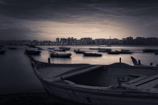 Fishing boat on the beach at sunrise with Alexandria skyline in far distance and cloudysky at sunrise