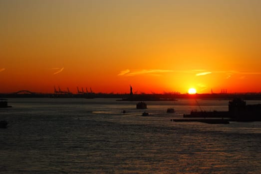 Silhouette of Statue of Liberty and Liberty Island in New York against an orange sunset sky