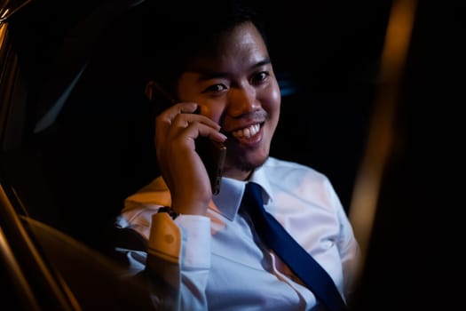 Businessman using smartphone in backseat of car near window at night, Handsome Asian young man work on late night sitting back seat and still work with mobile phone in city street
