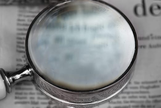 A magnifying glass, a reading aid lies on an old newspaper.