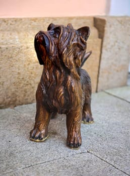 A wooden dog figure stands in front of a house on the sidewalk.