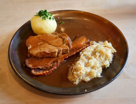 On a plate are a potato dumpling, slices of roast pork and sauerkraut.