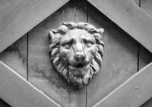 A lion head made of wood as a relief on a wooden gate.