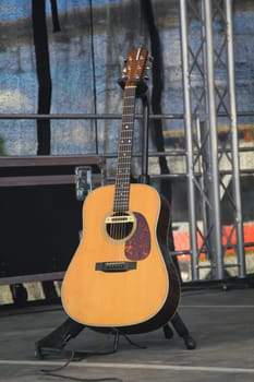 A guitar stands on a stage in its stand ready to hand.