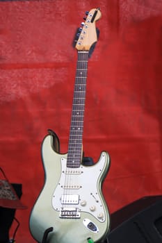 A guitar stands on a stage in its stand ready to hand.