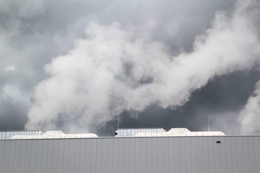 Dark clouds with water vapor over the building of a factory.