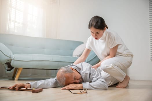 Asian elderly old man with walking stick fall on ground and granddaughter camp to help to support at home in living room, young woman halping her grandfather after falling down on floor, dizziness