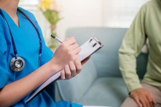 Asian young nurse writing prescription during home visit sick elder old man, Senior man takes doctor at home telling about health complaints, health care and medical concept