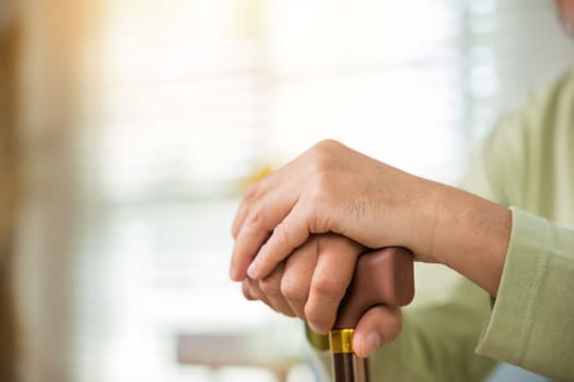 Closeup hands of senior disabled man holding walking stick, Old man sitting resting on sofa hold wooden walking cane, Elderly hand holding handle of cane, International Day for the Elderly