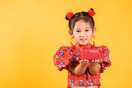 Chinese New Year. Happy Asian Chinese little girl smile wearing red cheongsam holding gift box, Portrait children in traditional dress hold, studio short isolated on yellow background