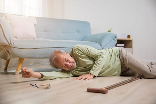 Asian old man lying on floor after falling down with wooden walking stick, Sick senior man beside couch on rug in living room at home, Elderly having an accident after doing physical therapy alone