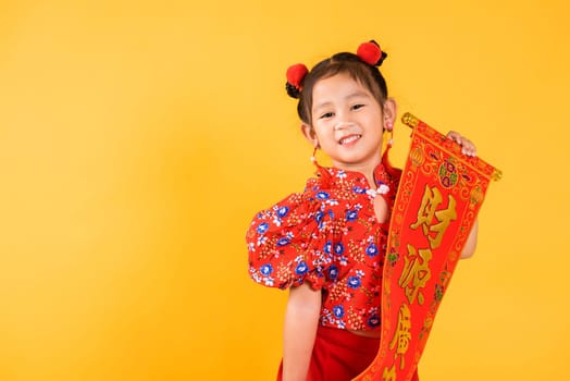 Chinese New Year. Happy Asian Chinese little child girl smile wearing red cheongsam qipao Spring festival couplets (Character "FU"" means fortune, blessing), studio short isolated on yellow background"
