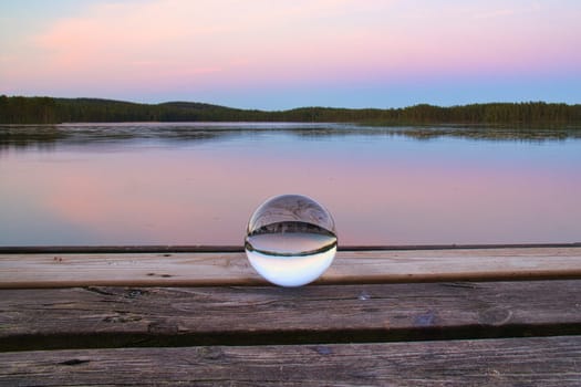 Glass ball on a wooden pier at a Swedish lake at evening hour. Nature shot from Scandinavia