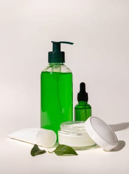 Refillable Cosmetic bottles, jar and tube near green leaves on white, bottles filled with green liquid, close up, mockup. Skincare beauty products. Natural cosmetics with aloe vera..