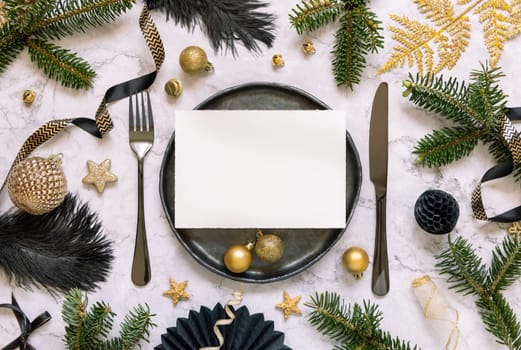 Black and golden Table setting with ornaments and fir tree branches top view, invitation card mockup. Christmas or New Year atmospheric composition on marble table, copy space.