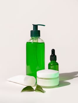 Refillable Cosmetic bottles, jar and tube near green leaves on white, bottles filled with green liquid, close up, mockup. Skincare beauty products. Natural cosmetics with aloe vera..
