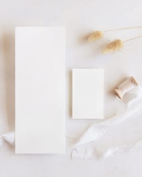 Blank cards near silk ribbons and dried hare's tail grass top view on white, mockup. Boho romantic scene with vertical cards. Bohemian or close to nature greeting or wedding Invitation