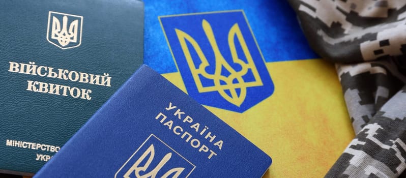 Ukrainian military ID and foreign passport on fabric with texture of pixeled camouflage. Cloth with camo pattern in grey, brown and green pixel shapes with Ukrainian army personal token and passport.