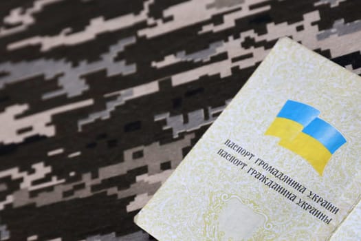Ukrainian foreign passport on fabric with texture of military pixeled camouflage. Cloth with camo pattern in grey, brown and green pixel shapes and Ukrainian ID close up