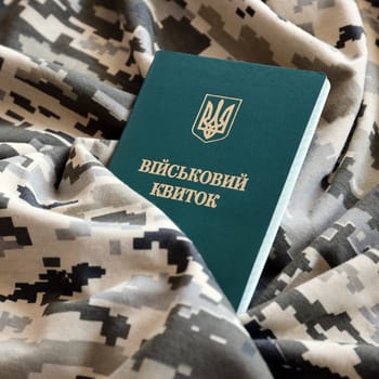 Ukrainian military ID on fabric with texture of pixeled camouflage. Cloth with camo pattern in grey, brown and green pixel shapes with Ukrainian army personal token close up.