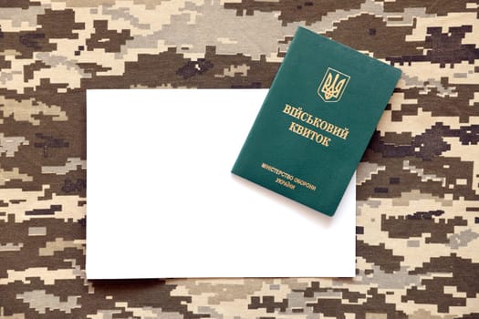 Ukrainian military ID and blank paper sheet on fabric with texture of pixeled camouflage. Cloth with camo pattern in grey, brown and green pixel shapes with Ukrainian army personal token close up.