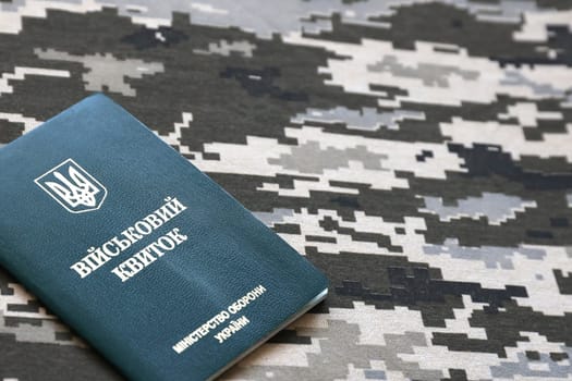 Ukrainian military ID on fabric with texture of pixeled camouflage. Cloth with camo pattern in grey, brown and green pixel shapes with Ukrainian army personal token close up.