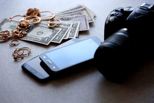 Many expensive golden jewerly rings, earrings and necklaces with big amount of US dollar bills close to smartphones and digital slr camera. Pawn shop concept