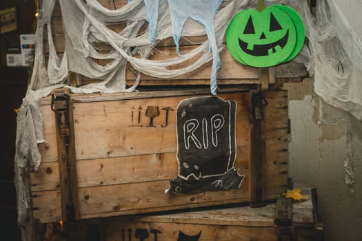 Green bright halloween pumpkin with painted nose, mouth and eyes on wooden box with gauze as web and tombstone with RIP inscription. Handmade images of scary face and grave. DIY Halloween decoration