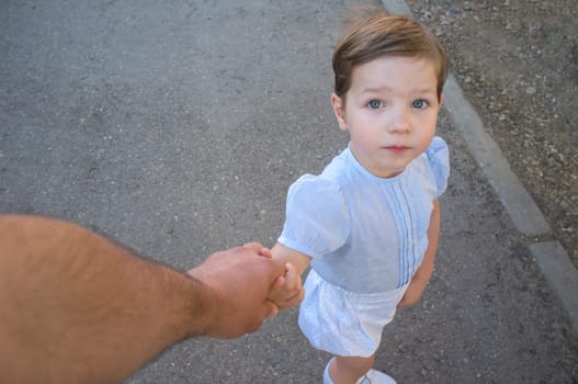 3-year-old boy holds his father's hand to cross the street. Point of view shot