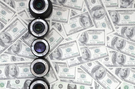 A few photographic lenses lies on the background of a lot of dollar bills. Space for text