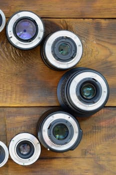 Several photographic lenses lie on a brown wooden background. Space for text
