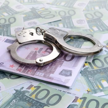 Police handcuffs lies on a set of green monetary denominations of 100 euros. A lot of money forms an infinite heap