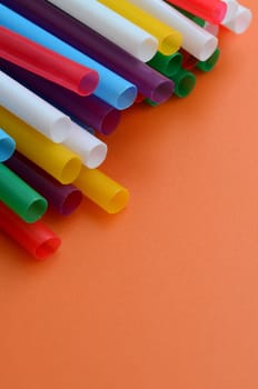 Many colorful straws for drinks lies on a bright orange background surface