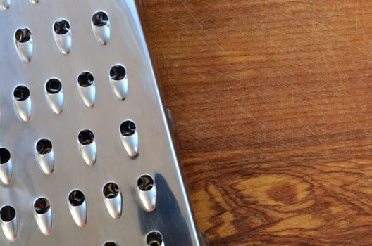 The chrome grater lies on the cutting board with a lot of scars from the ax and knife. Background image for cooking recipes