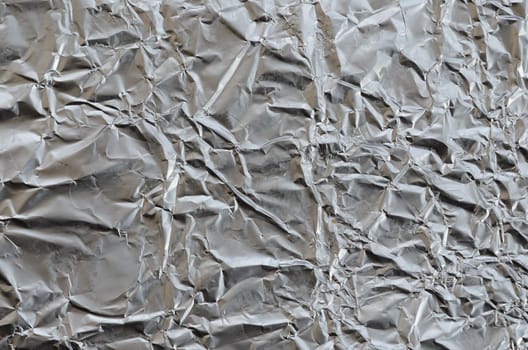 Thin wrinkled sheet of crushed tin aluminum silver foil background with shiny crumpled surface for texture