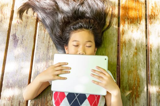 The girl sleep while playing tablet pc on wooden bed.