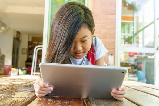 The girl lying on wooden bed with playing tablet pc.