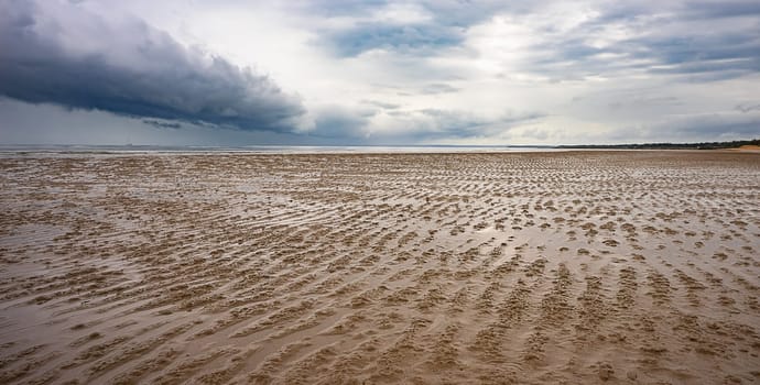 Sand flats of the intertidal zone of Pialba Beach, Queensland, at low tide with a storm approaching Hervey Bay.