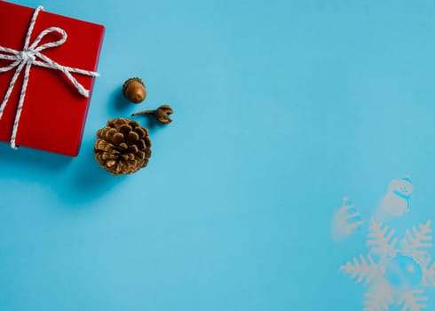 Christmas background of red gifts box with white and silver cord rope ribbon, conifer cones, and acorn on blue paper background. Flat layout with copy space design.